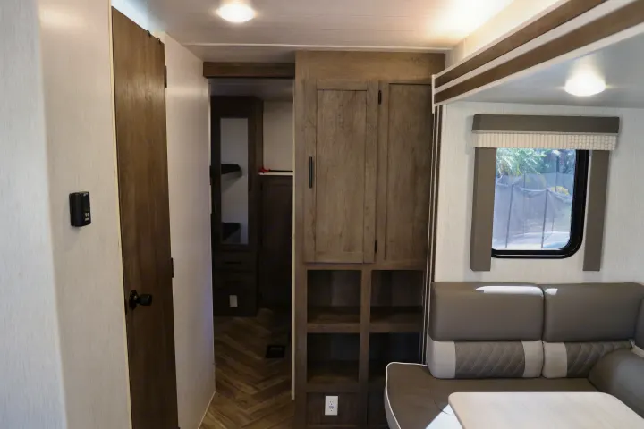 Interior of an RV rental, showing a modern dinette, wood-look storage, thermostat, and bunk beds visible through a doorway.. Forest River Salem Cruise Lite 2022