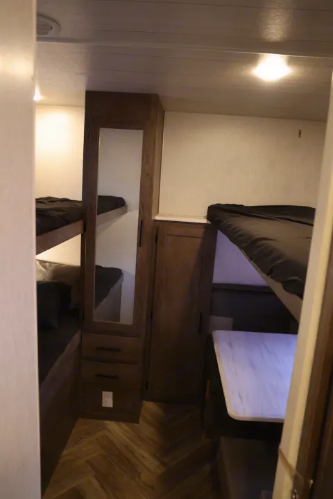 This RV rental interior shows dark bunk beds, a mirrored cabinet, and a white dinette table on herringbone flooring.. Forest River Salem Cruise Lite 2022