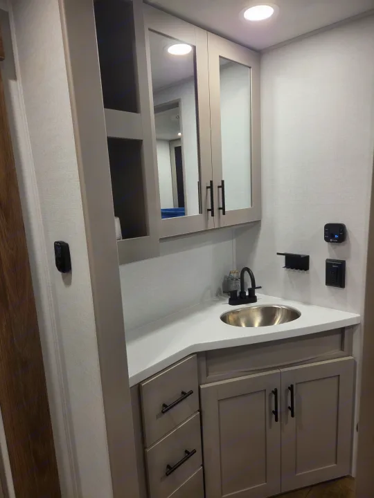 Inside a clean RV rental: modern bathroom vanity with light gray cabinets, stainless sink, black faucet, and mirrored storage.. Alliance RV Delta 2026