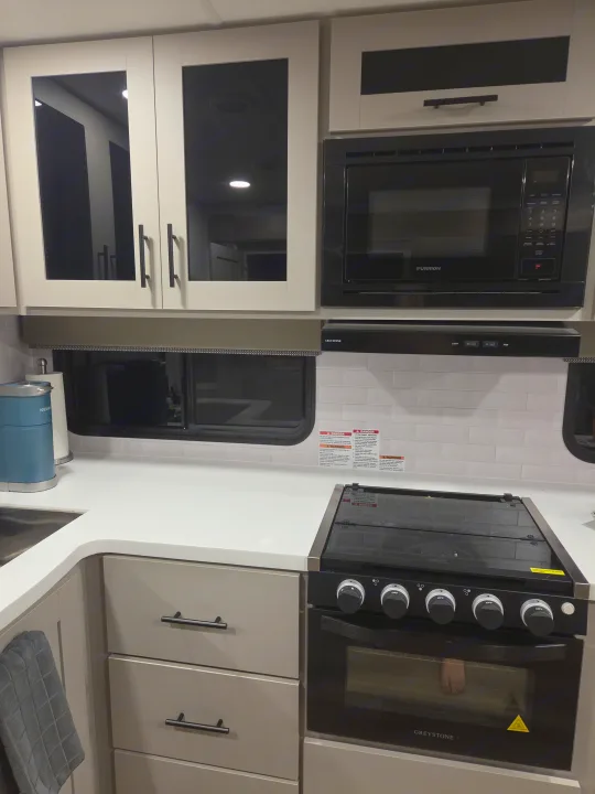 Modern RV rental kitchen featuring white subway tile backsplash, microwave, Greystone stove, and Keurig on countertops.. Alliance RV Delta 2026