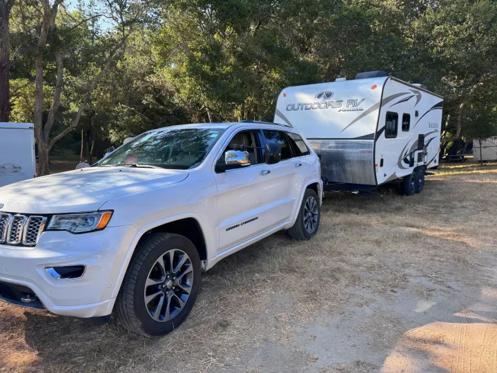 White Jeep Grand Cherokee towing a white Outdoors RV Black Rock trailer, perfect for an RV rental getaway.. Outdoors RV Blackrock 2017