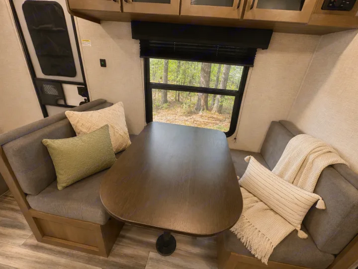 Explore this inviting RV rental dinette: grey benches with pillows, wooden table, and a window offering tranquil forest views.. Jayco Jay Flight SLX 2025