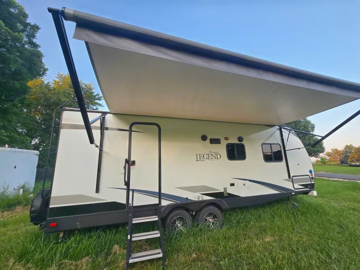 White travel trailer RV rental with an extended awning, parked on green grass under a clear sky, ready for outdoor adventures.. Forest River Surveyor Legend 2020