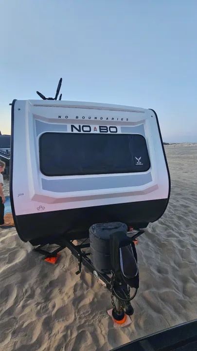 Front of a white and black NoBo travel trailer on a sandy beach. An rv rental ready for your next adventure.. No Boundaries 19 2022