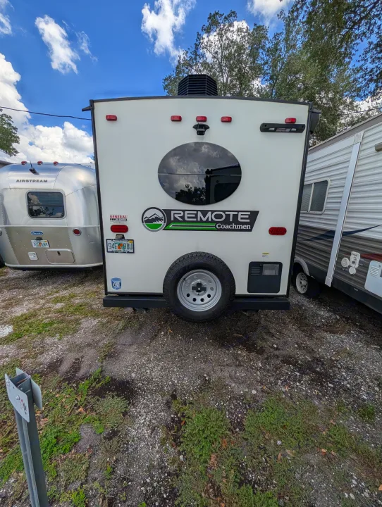 Rear of a white 'REMOTE Coachmen' RV rental, featuring a spare tire & Florida plate, with an Airstream nearby for camping.. Coachmen Other 2024