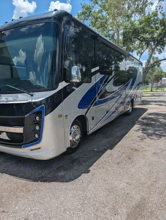 Sleek silver, black, and blue motorhome rv rental parked on a sunny day, reflecting clouds, ready for adventure.. Entegra Coach Vision XL 2022