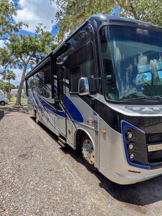 This modern black, silver, and blue motorhome is parked on gravel, an excellent rv rental for your next outdoor adventure.. Entegra Coach Vision XL 2022
