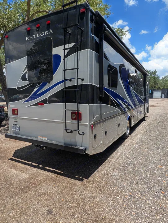 This large black, grey, and blue Entegra RV rental, with a ladder and storage, is parked on gravel, ready for adventure.. Entegra Coach Vision XL 2022