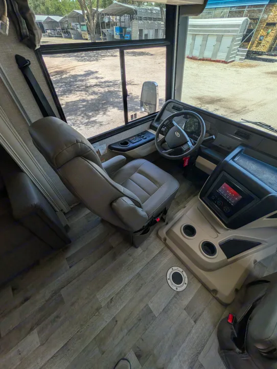 RV rental interior: driver's cabin with steering wheel, dashboard, infotainment screen, and view of covered storage units.. Entegra Coach Vision XL 2022
