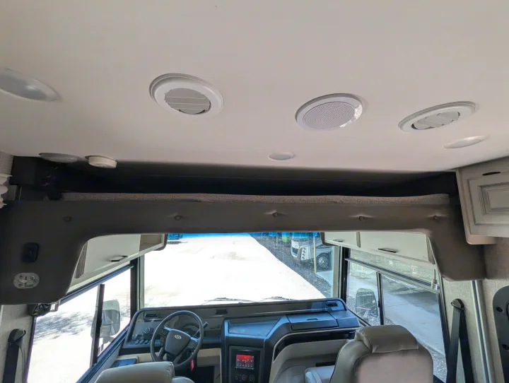 RV rental cockpit interior, showing the dashboard, steering wheel, front seats, overhead bunk, and ceiling fixtures.. Entegra Coach Vision XL 2022