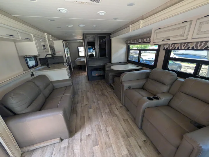 Modern RV rental interior with recliners, dinette, kitchen, and a glimpse of the bedroom, featuring wood-look flooring.. Entegra Coach Vision XL 2022