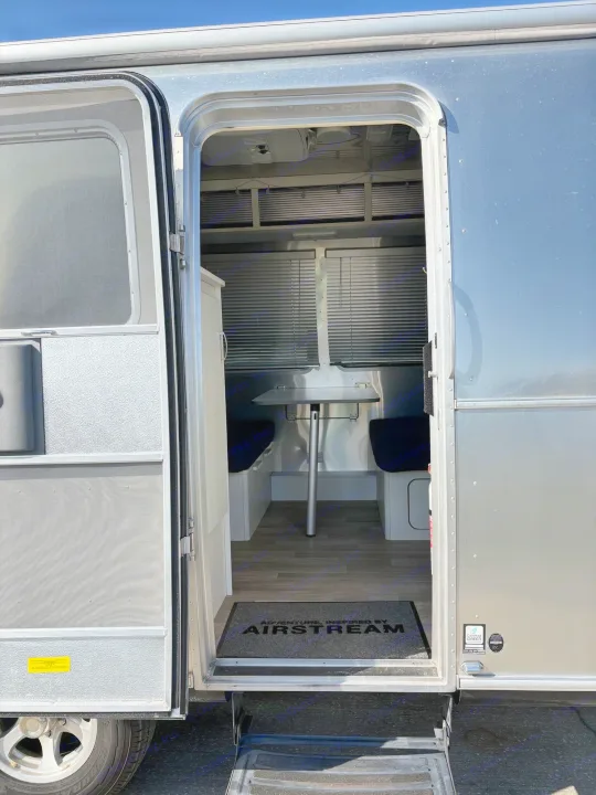 Step inside this Airstream RV rental! Its open door reveals a cozy interior with a dinette, table, and dark benches.. Airstream Bambi 2022
