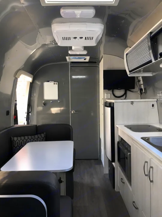 Modern rv rental interior featuring a bright kitchen, cozy dining booth, and sleek ceiling with AC. Ready for adventure!. Airstream Sport 2019