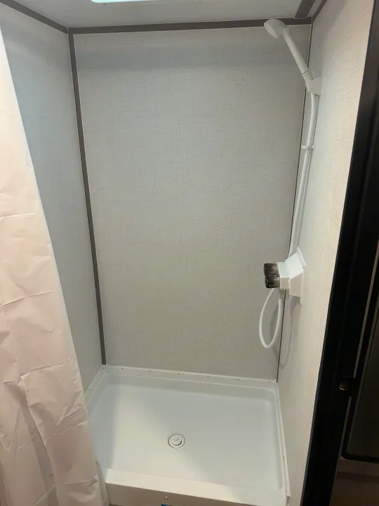 This clean, compact shower in an RV rental features an adjustable shower head and water controls. The white shower pan is ready for use.. Keystone RV Aspen trail 2024