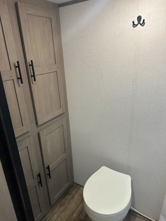 Compact RV rental bathroom featuring a white toilet, light wood cabinets, textured grey walls, and a playful octopus hook.. Keystone RV Aspen trail 2024