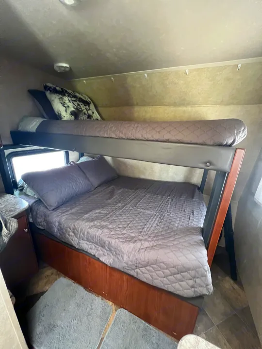 Cozy RV rental sleeping area featuring two bunk beds with matching grey bedding, ideal for travel.. Forest River Wildwood X-Lite FS 2015