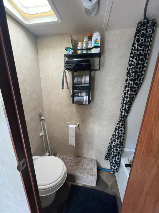 This compact RV rental bathroom features a toilet, shower with a black patterned curtain, toiletries, and neatly folded towels, optimizing space.. Forest River Wildwood X-Lite FS 2015