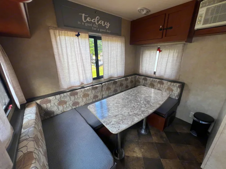 Inviting RV rental interior featuring a U-shaped dinette with patterned cushions, a light table, and windows with sheer curtains.. Forest River Wildwood X-Lite FS 2015