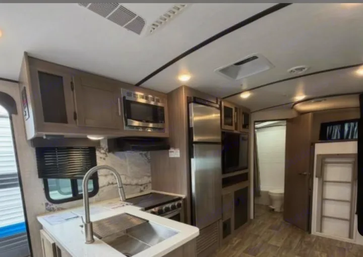 Modern RV rental interior with full kitchen (sink, microwave, stove, fridge), bathroom, & bunk beds.. Crossroads RV Sunset Trail Super Lite 2022