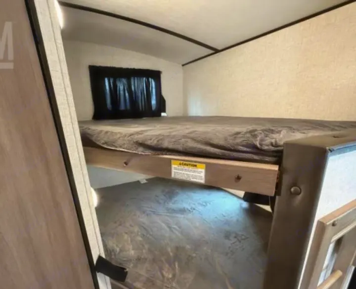 Compact RV rental sleeping area featuring bunk beds with grey bedding and a window. Ideal for a family camper.. Crossroads RV Sunset Trail Super Lite 2022