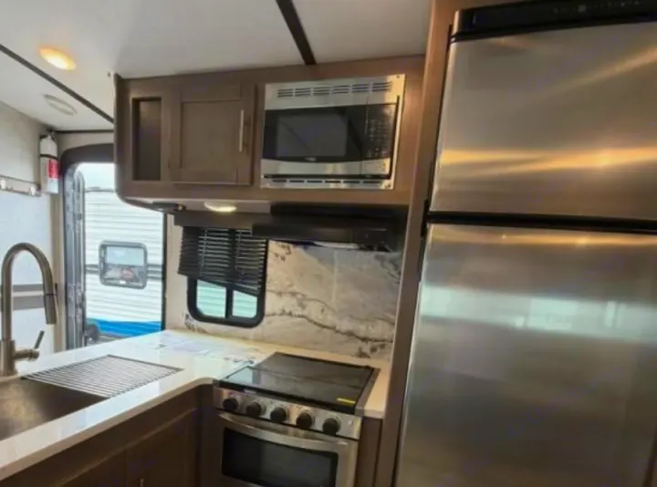 Modern RV rental kitchen featuring stainless steel fridge, microwave, and stove. Includes sink, ample counter space & cabinets.. Crossroads RV Sunset Trail Super Lite 2022