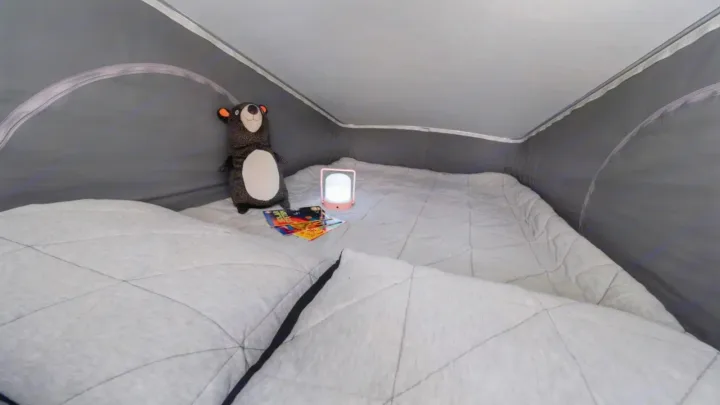 Inside a cozy RV rental: a grey quilted mattress, plush bear, books, and a glowing night light. Ideal for camper adventures.. Winnebago Solis 2023