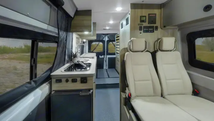 RV rental interior: A compact kitchen with sink and fridge, two passenger seats, and control panels.. Winnebago Solis 2023