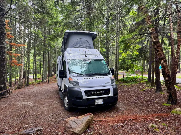Forest rv rental adventure: White pop-top camper van parked at a shaded campsite among pines.. Winnebago Solis 2023