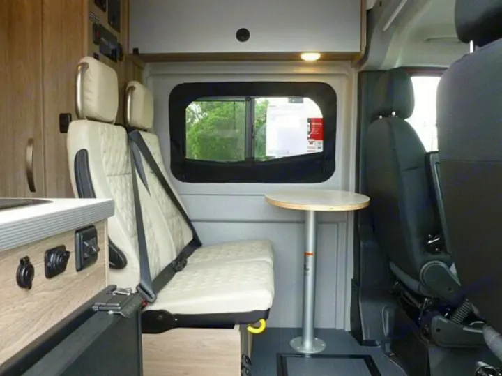 RV rental interior: a cozy camper van seating area with a small table, window, and wall-mounted controls.. Winnebago Solis 2023