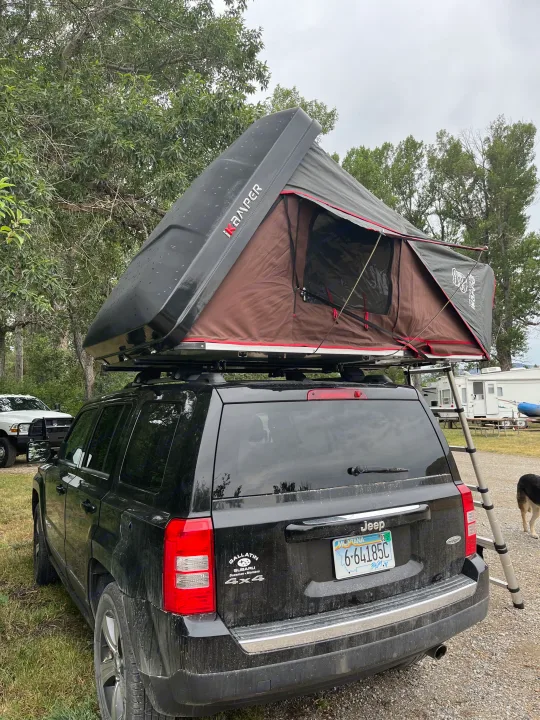 Black Jeep Patriot SUV with a deployed iKamper rooftop tent, set up for camping. An exciting RV rental for outdoor adventures.. Other Jeep Patriot 2016