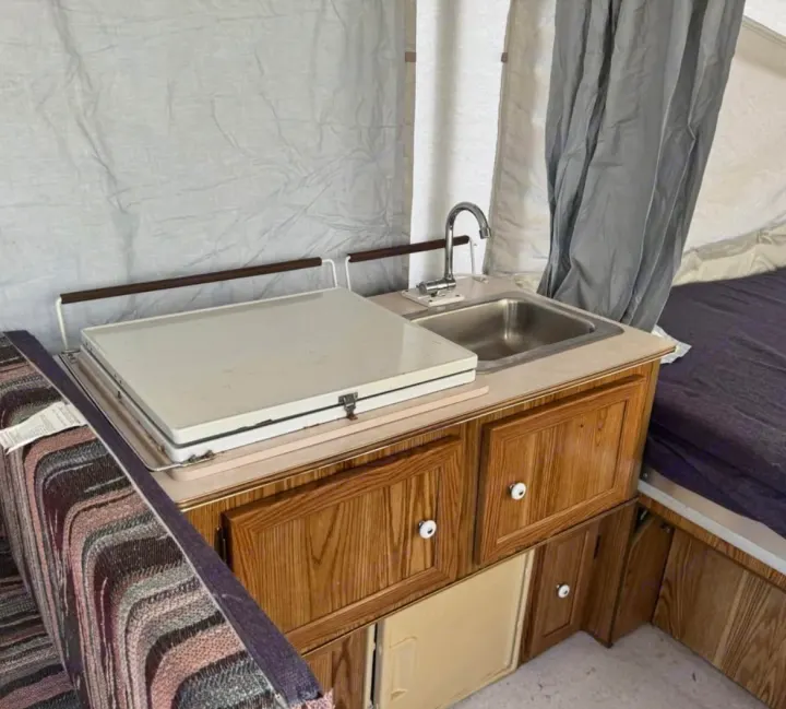 This RV rental pop-up camper features a compact kitchenette with a sink, faucet, and covered stovetop, ideal for travel camping.. Coleman Destiny Rio Grande 1995