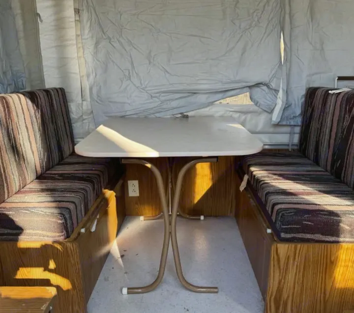 Inside an RV rental: a pop-up camper's dinette area featuring striped benches, a light table, and canvas walls.. Coleman Destiny Rio Grande 1995