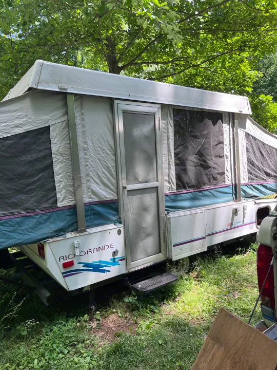 This pop-up rv rental, a Coleman Fleetwood Rio Grande, is set up in a lush green outdoor area, ready for adventure.. Coleman Destiny Rio Grande 1995