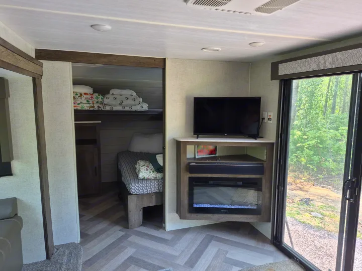 Spacious RV rental interior featuring bunk beds, an entertainment unit with TV & fireplace, and a scenic nature view.. Forest River Wildwood 2021