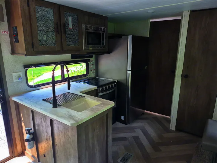 This rv rental features a modern kitchen with a sink, stove, microwave, and refrigerator, all within a brightly lit interior.. Forest River Wildwood 2021