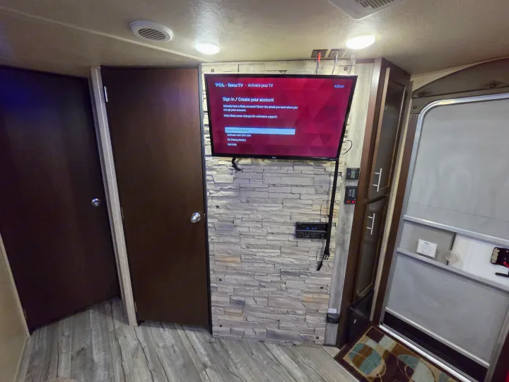 Compact rv rental interior with a Roku TV on a stone accent wall, featuring a stereo, controls, and doors.. Forest River Cherokee 2017