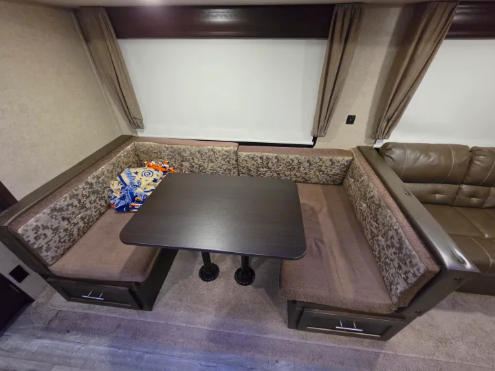Comfortable RV rental dinette featuring U-shaped seating, storage, patterned cushions, and an adjacent brown leather sofa.. Forest River Cherokee 2017