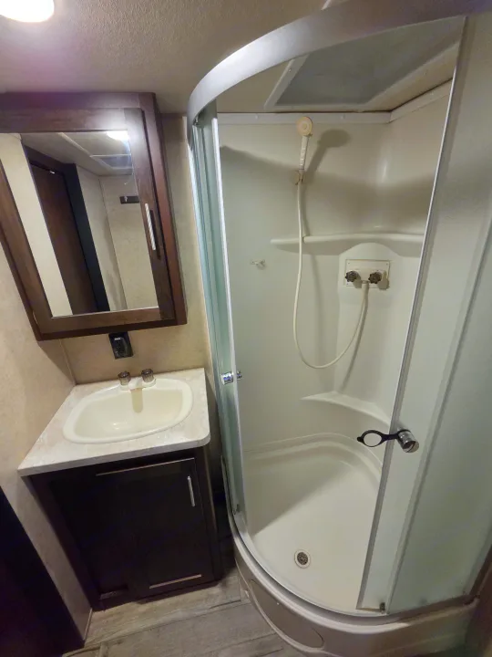 Compact RV rental bathroom featuring a corner shower, sink vanity, and mirrored medicine cabinet.. Forest River Cherokee 2017