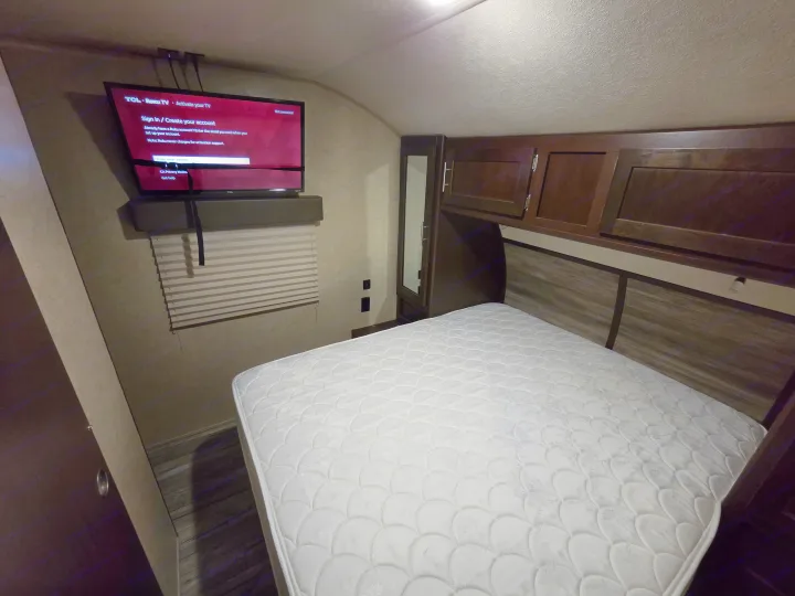 This RV rental bedroom features a comfortable white bed, overhead dark wood cabinets, and a TCL Roku TV displaying its activation screen.. Forest River Cherokee 2017