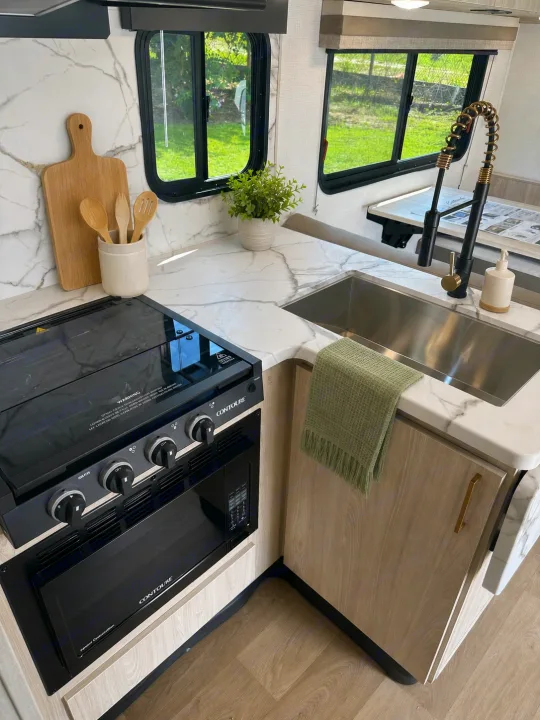 Modern RV rental kitchen featuring sleek countertops, black appliances, and light wood cabinets. Perfect for your next adventure!. East to West Entrada 2026