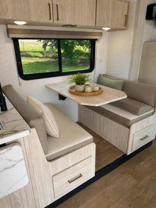 Modern rv rental dinette: light wood, comfy bench seating, natural decor, and a scenic window view of greenery.. East to West Entrada 2026