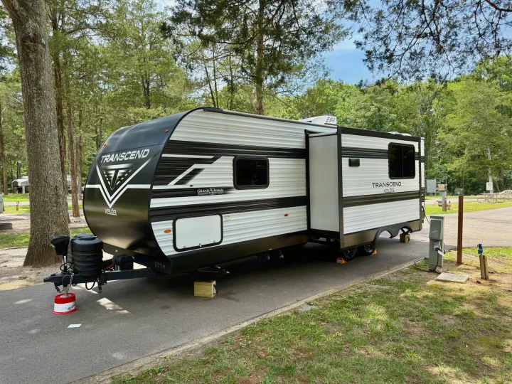 A Grand Design Transcend Xplor RV rental is parked at a shaded campsite, its slide-out extended. Ready for camping!. Grand Design Transcend Xplor 2025