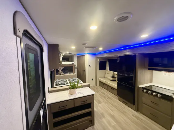 Modern RV rental interior with kitchen, bunk beds, and lounge seating, featuring blue LED lighting.. Grand Design Transcend Xplor 2025