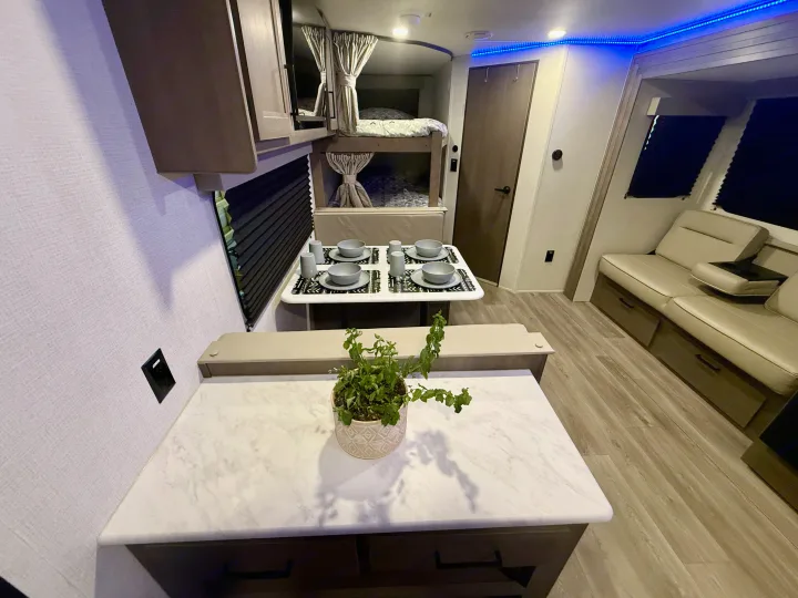 Modern RV rental interior showing a dining area, bunk beds, comfortable seating, and blue ambient lighting.. Grand Design Transcend Xplor 2025