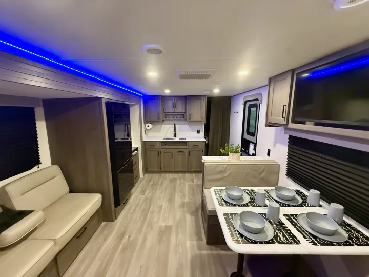Modern rv rental interior showcasing a kitchen, dinette, and sofa with blue accent lighting and wood-look floors.. Grand Design Transcend Xplor 2025