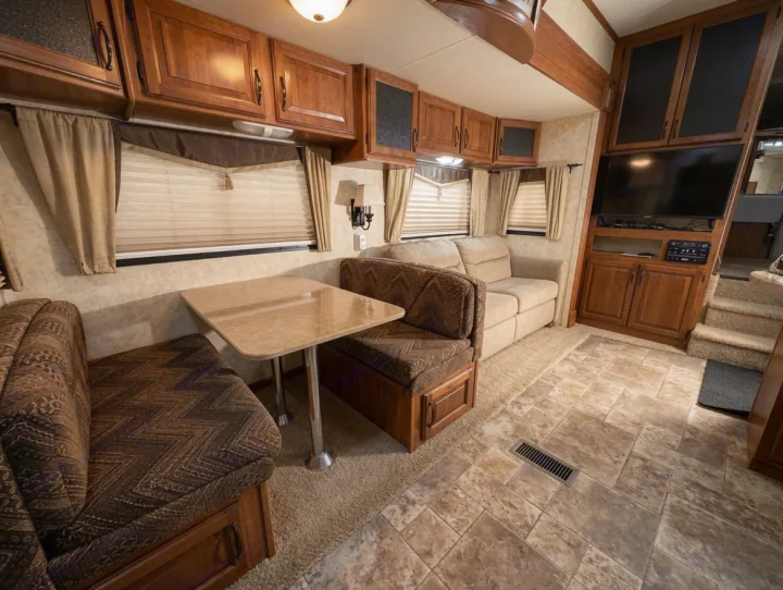 Cozy RV rental interior with a dining booth, sofa, entertainment center, and steps to a bedroom area. Warm, neutral tones.. Keystone RV Montana High Country 2010