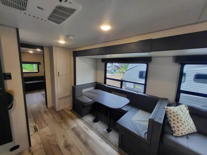 RV rental interior featuring a dinette with booth seating, table, and sofa. Wood-look floors and windows showing outside.. KZ Sportsmen SE 332bkhse 2022