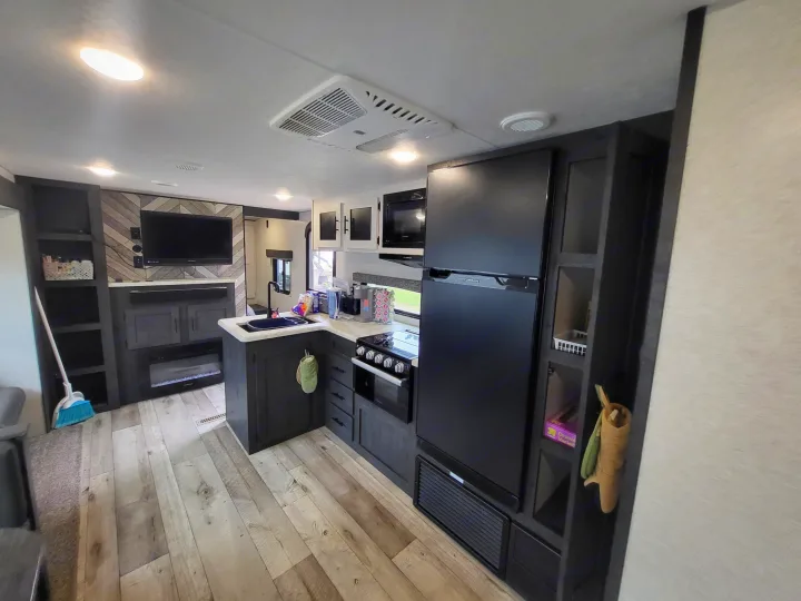 Spacious rv rental kitchen and living area, featuring a modern design with dark cabinets, full fridge, stove, and TV.. KZ Sportsmen SE 332bkhse 2022