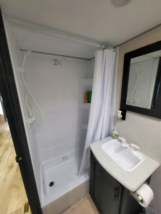 Compact RV rental bathroom with a white shower, handheld showerhead, sink vanity, and mirror. Practical and functional.. KZ Sportsmen SE 332bkhse 2022