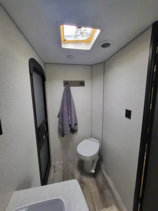 Inside a clean rv rental bathroom: compact toilet, sink, overhead fan, and towel. Features light walls and wood-look floor.. KZ Sportsmen SE 332bkhse 2022